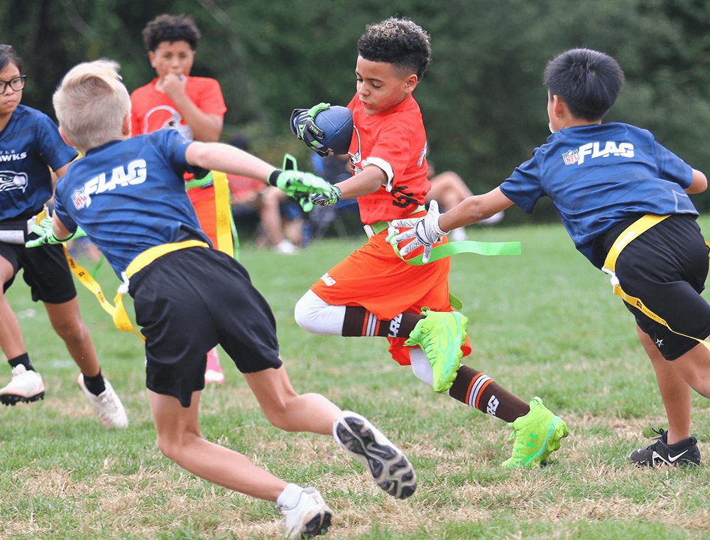 A ball carrier in orange cuts past defenders in blue
