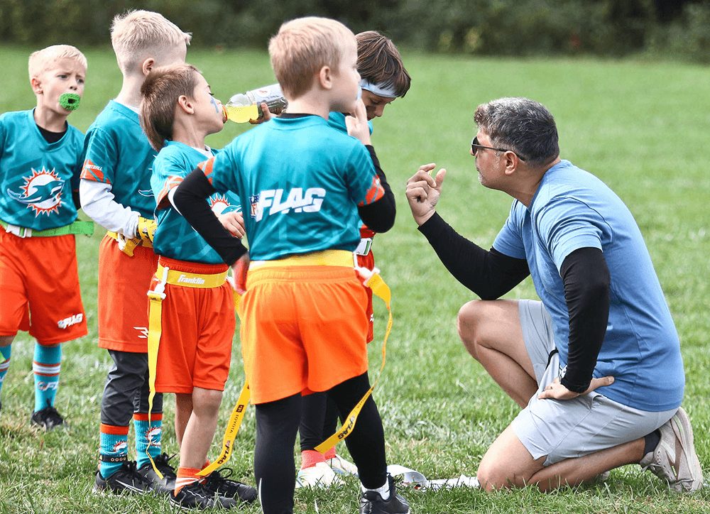 A coach kneels to teach young players in Dolphins jerseys