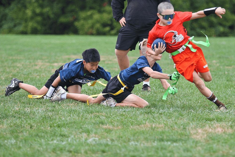 A defender dives for a flag as a ball carrier in orange runs upfield