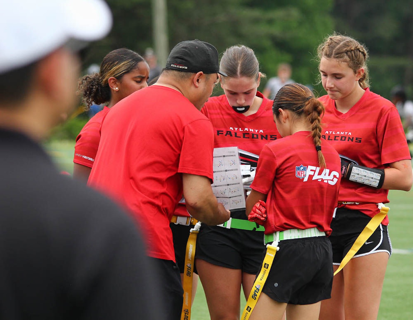 A coach with a clipboard huddles with an All-Girls team