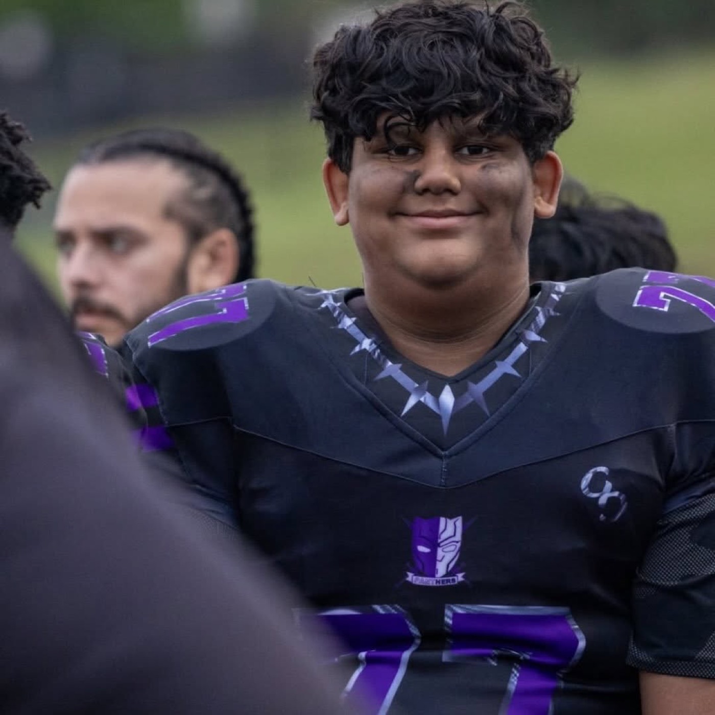 A smiling Panthers lineman in a black and purple jersey on the sideline