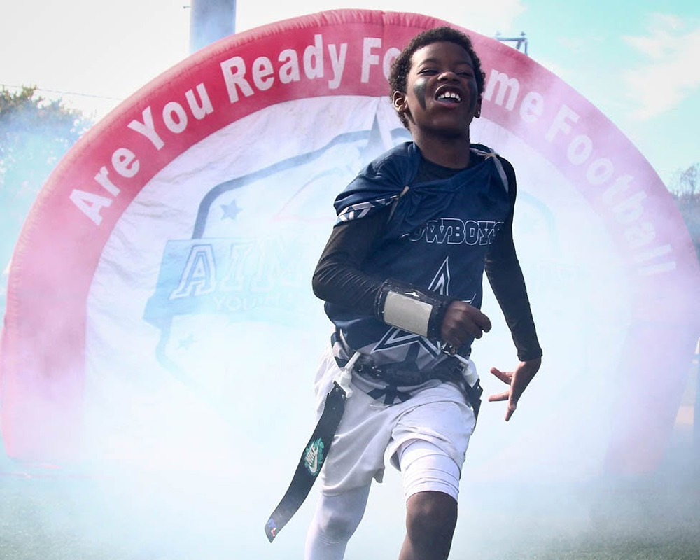 A player in a Cowboys jersey sprints out of the smoke-filled Aim High tunnel on game day